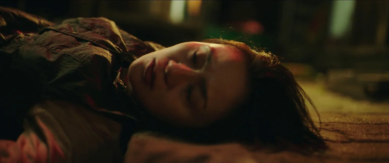 Psychokinesis (2018) movie still: closeup — A dark indoor space with the floor visible as a blurred textured surface. A young woman lies…