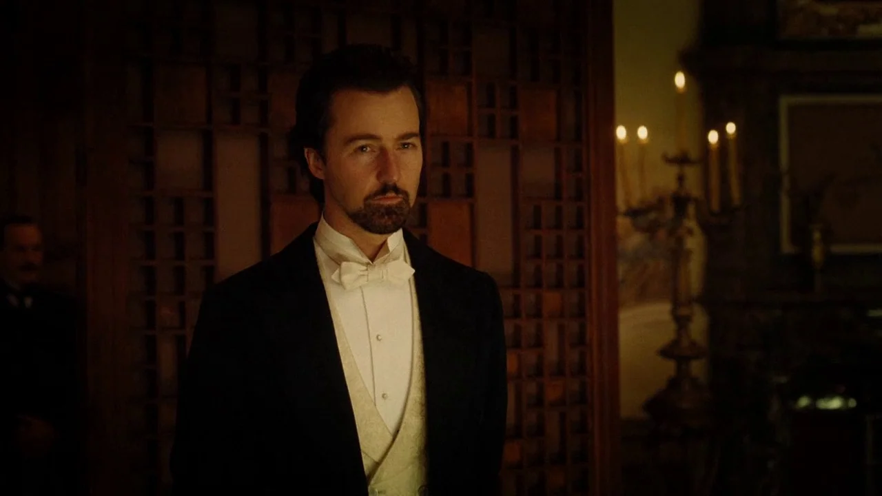 The Illusionist (2006) movie still: medium — A dimly lit room features dark wood paneling and a blurred candelabra in background. A man in formal…