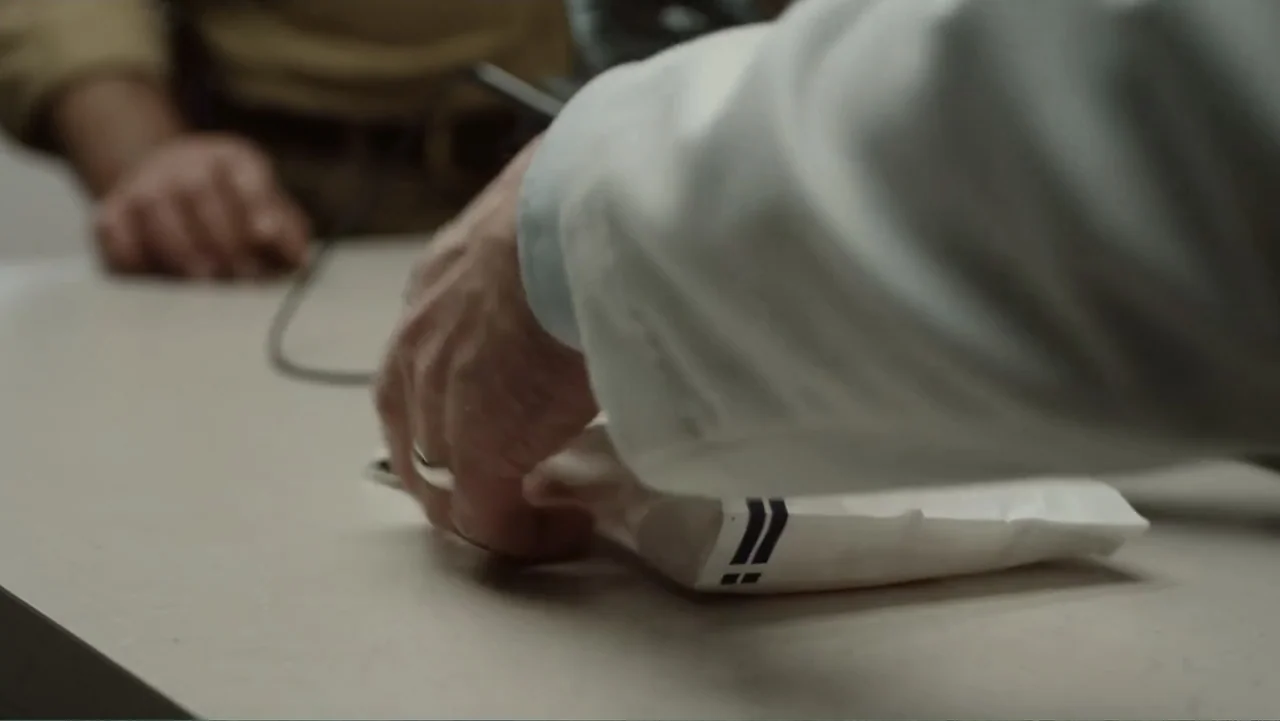 The Cleaner (2021) movie still: closeup — A light-colored countertop surface holds a small paper parcel with blue branding. A person's hand wearing…