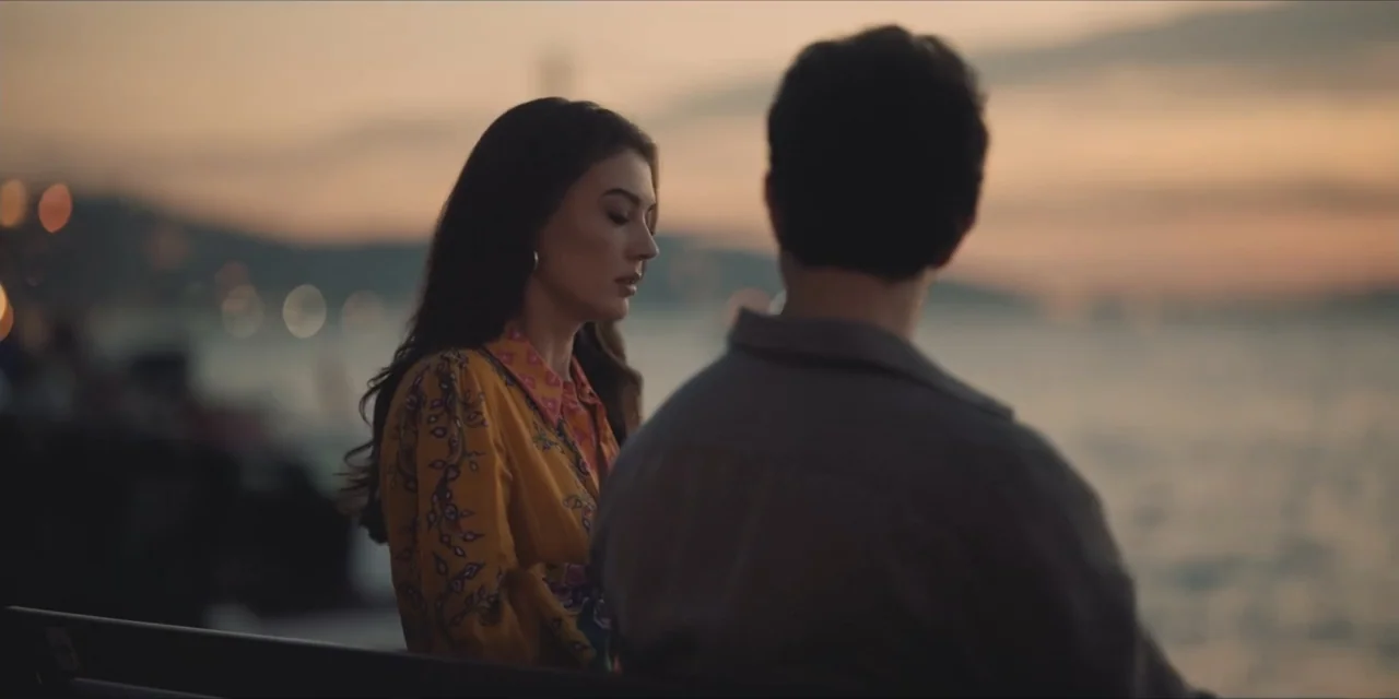 Kill Me If You Dare (2019) movie still: medium — A waterfront promenade at sunset with a calm body of water in the background. A young woman and a…