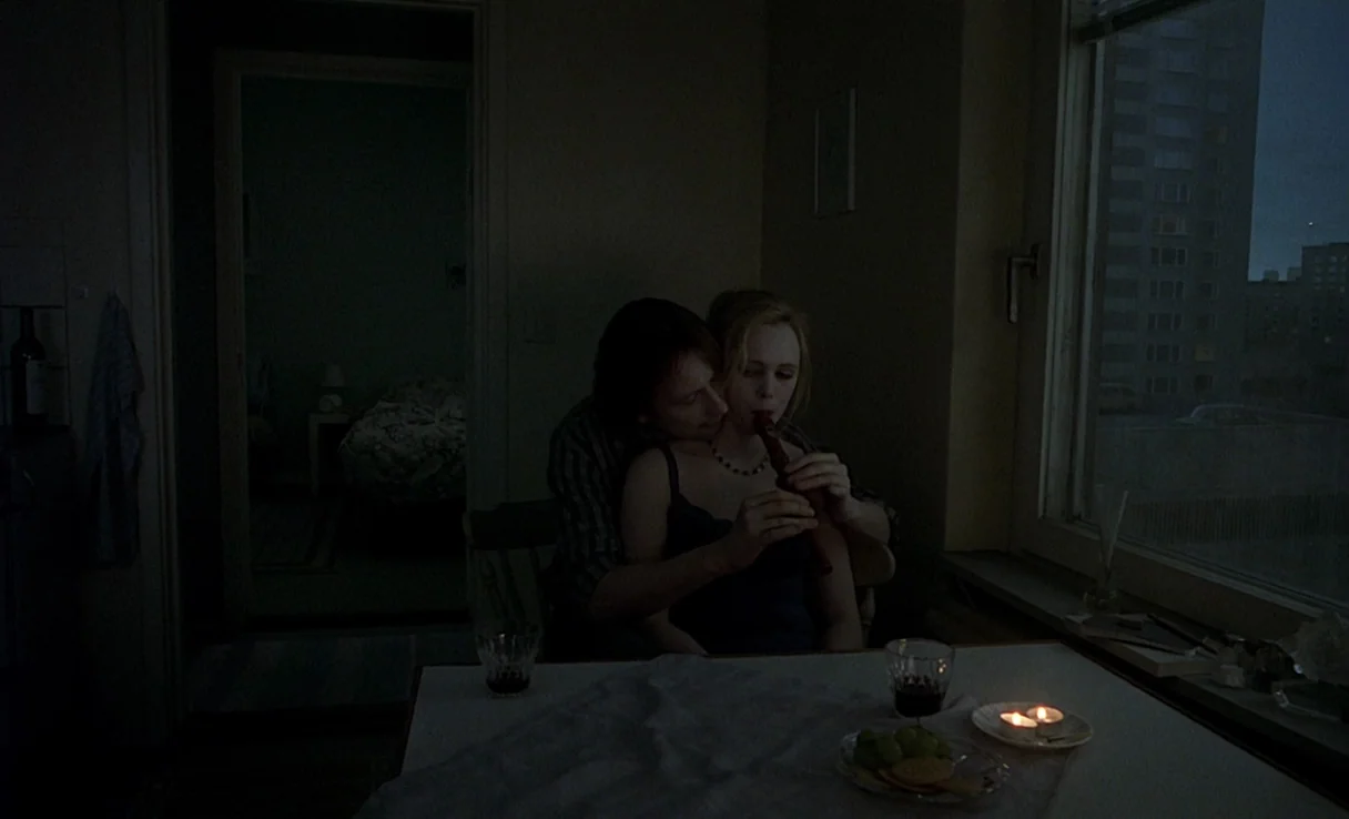 Songs from the Second Floor (2000) movie still: medium — A dark, sparsely furnished room features a window overlooking high-rise city apartment…