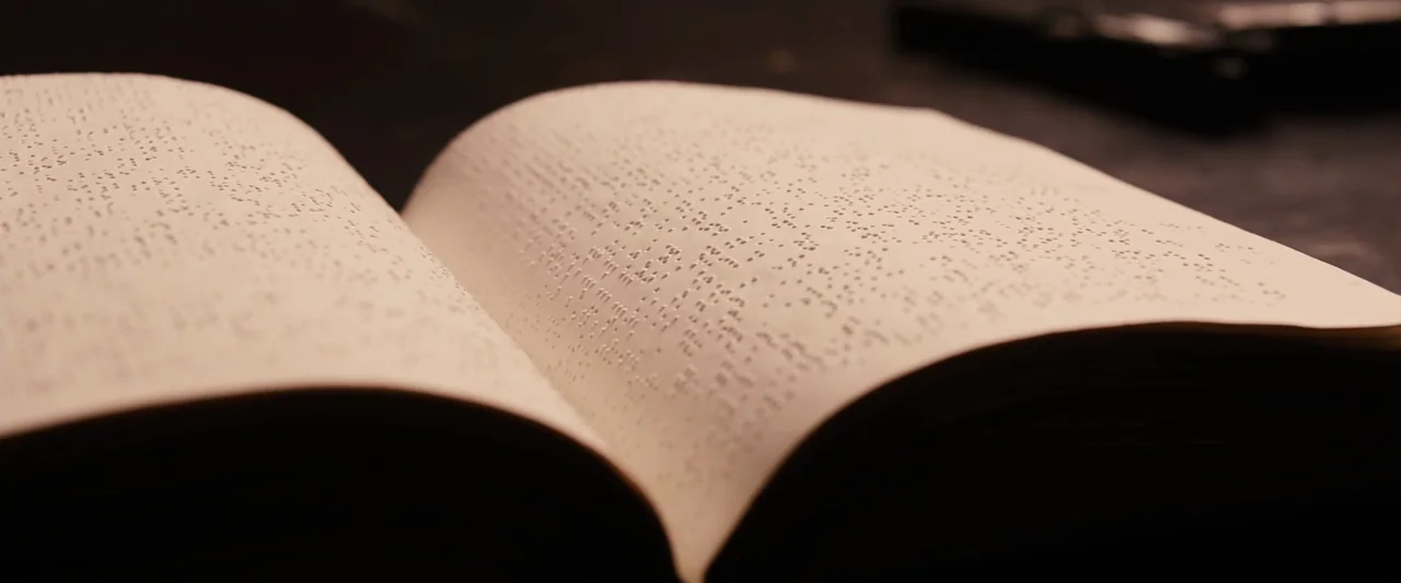 The Book of Eli (2010) movie still: closeup — An open book with raised braille lettering rests on a dark, indistinct surface. The pages are curved…