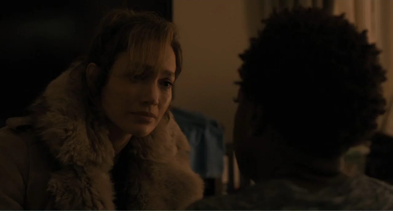 Lila & Eve (2015) movie still: medium — A dimly lit indoor space with blurred furniture in the dark background. A woman in a fur-collared coat gazes…
