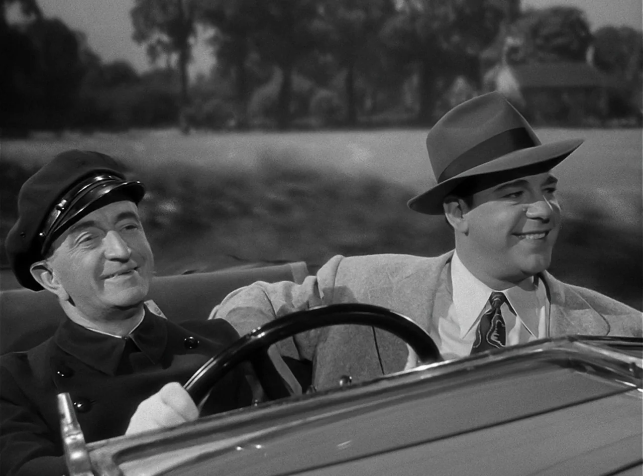 The Wolf Man (1941) movie still: medium — An older man driving a car and a younger man riding in the passenger seat. They are cruising along a road…