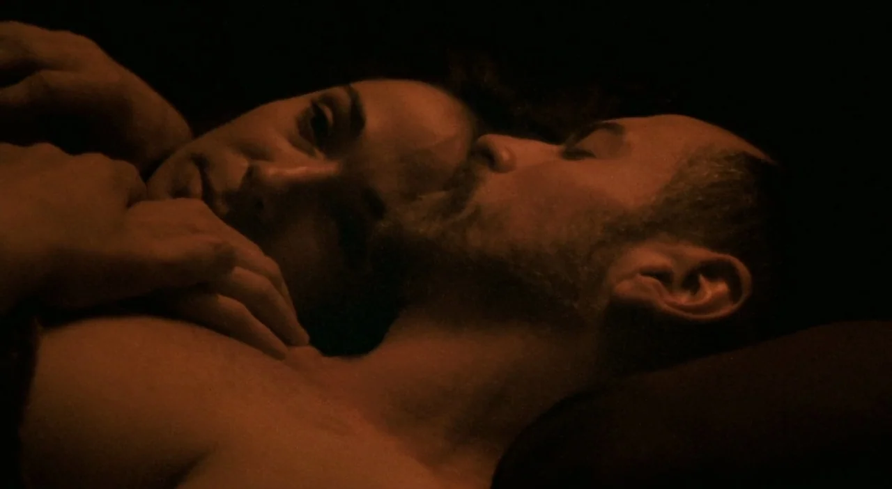 Patagonia (2010) movie still: closeup — A dark bedroom setting with a man and woman lying together in shadow. The man rests with eyes closed while…