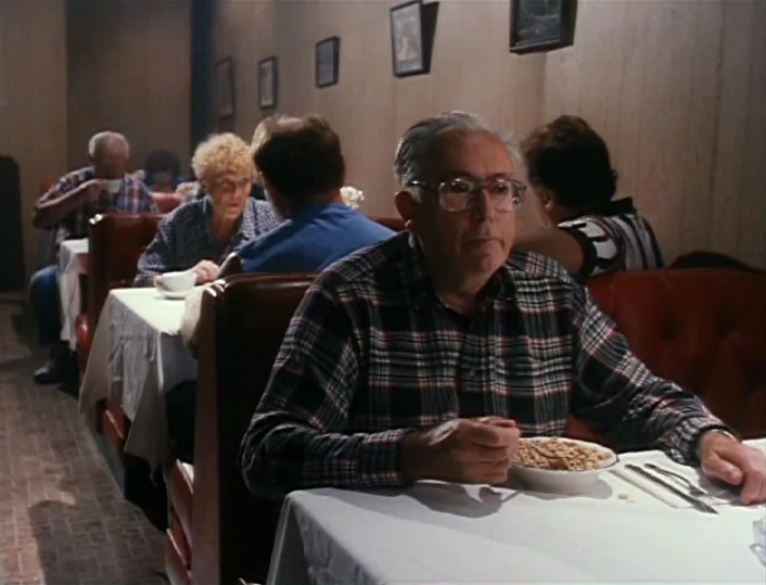Head of the Family (1996) movie still: medium — A diner interior with red vinyl booths and wood-paneled walls decorated with framed prints. An…