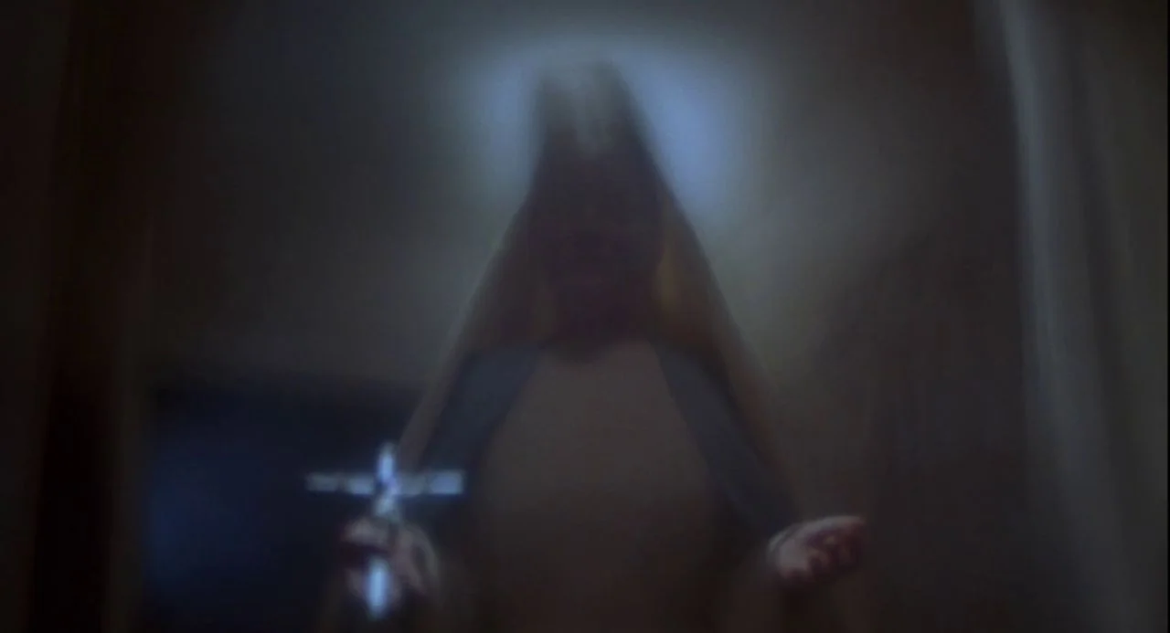 Psycho III (1986) movie still: medium — A dark interior room is filled with a soft glow around a figure. A woman wearing a nun's habit stands…