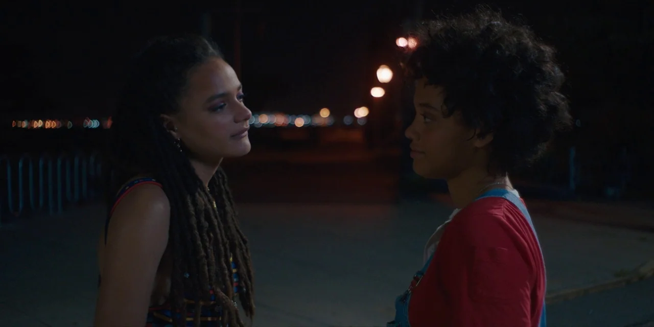 Hearts Beat Loud (2018) movie still: medium — Two women stand facing each other at night on a dark paved outdoor path. Distant out-of-focus…
