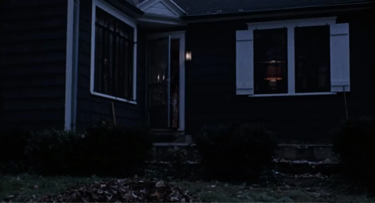 The Last House on the Left (2009) movie still: wide — A dark suburban house at night features a glowing window and open screen door. The exterior is…
