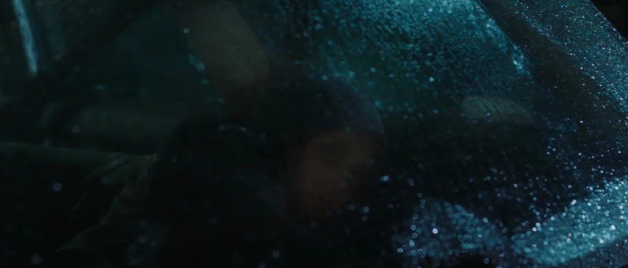 Wildlike (2014) movie still: medium — A dark car interior at night is viewed through a rain-covered windshield. A person sits in the driver seat…