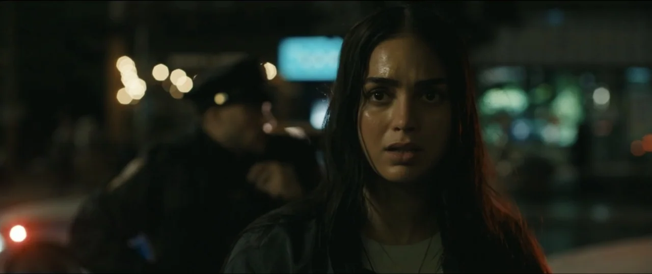 Scream VI (2023) movie still: closeup — A woman stands in a blurry urban night environment illuminated by distant city lights. She stares forward…