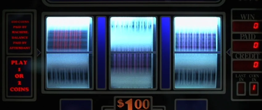 Hard Eight (1996) movie still: closeup — A close-up view of a slot machine interface with three vertically spinning internal reels. Glowing red text…