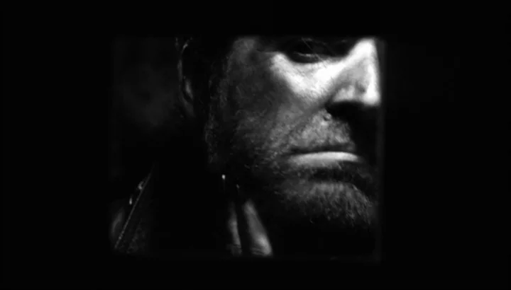 The American Astronaut (2001) movie still: closeup — A dark space frames the right half of a man's face in high contrast. The subject remains static…
