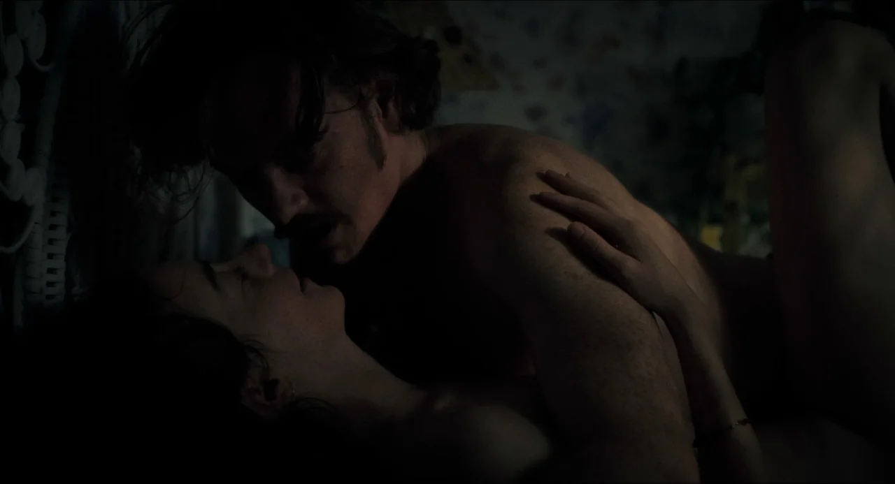 Happiness (1998) movie still: closeup — A dimly lit scene showing two people lying face-to-face in a dark room. The man with a mustache looks at the…