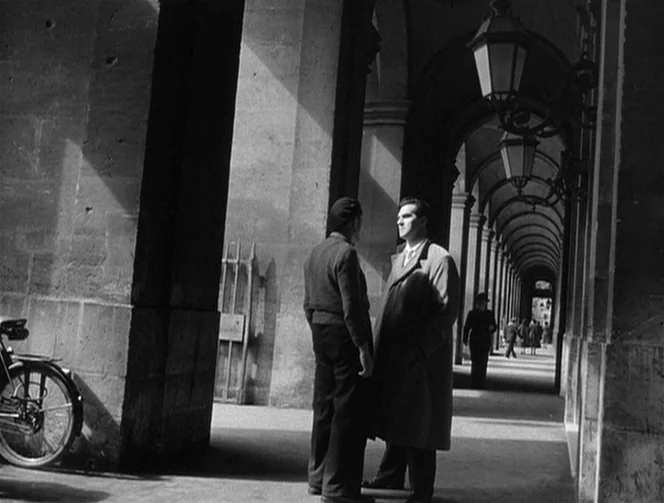 Mr. Arkadin (1955) movie still: fullbody — A long stone colonnade with repeating arches features men talking in the foreground. Another individual…