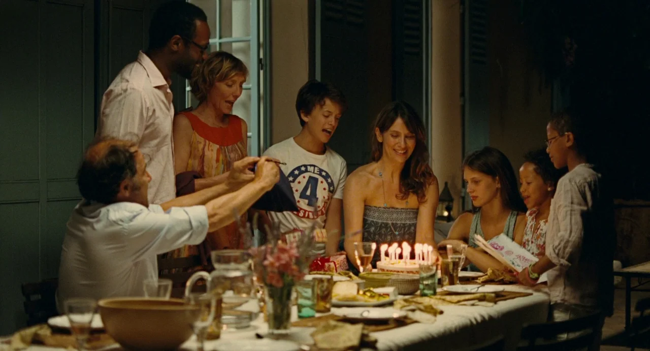 Young & Beautiful (2013) movie still: medium — A group gathers around a dining table at night to celebrate a birthday. A cake with lit candles sits…