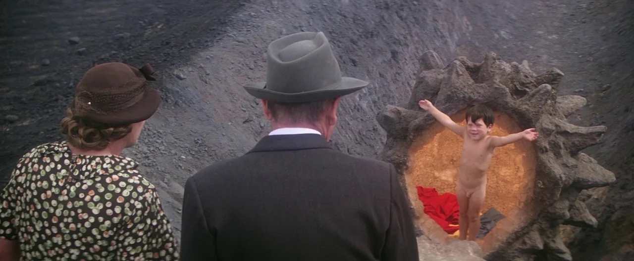 Superman (1978) movie still: wide — A man and woman stand before a jagged volcanic formation with an illuminated center. A young child with arms…