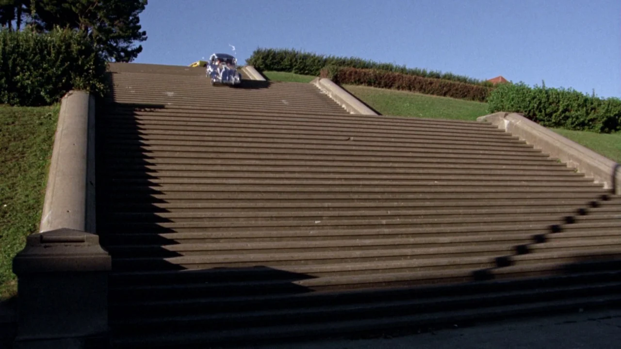What’s Up, Doc? (1972) movie still: wide — A wide concrete staircase sits between grassy embankments under a clear blue sky. A silver vintage car…