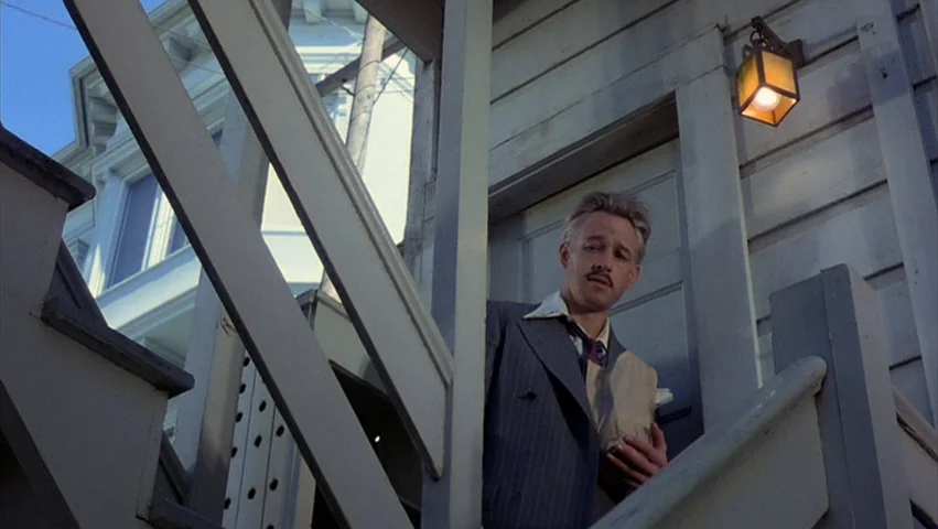 Hammett (1982) movie still: medium — An outdoor wooden stairway connects to the clapboard exterior of a residential building. A man in a suit…
