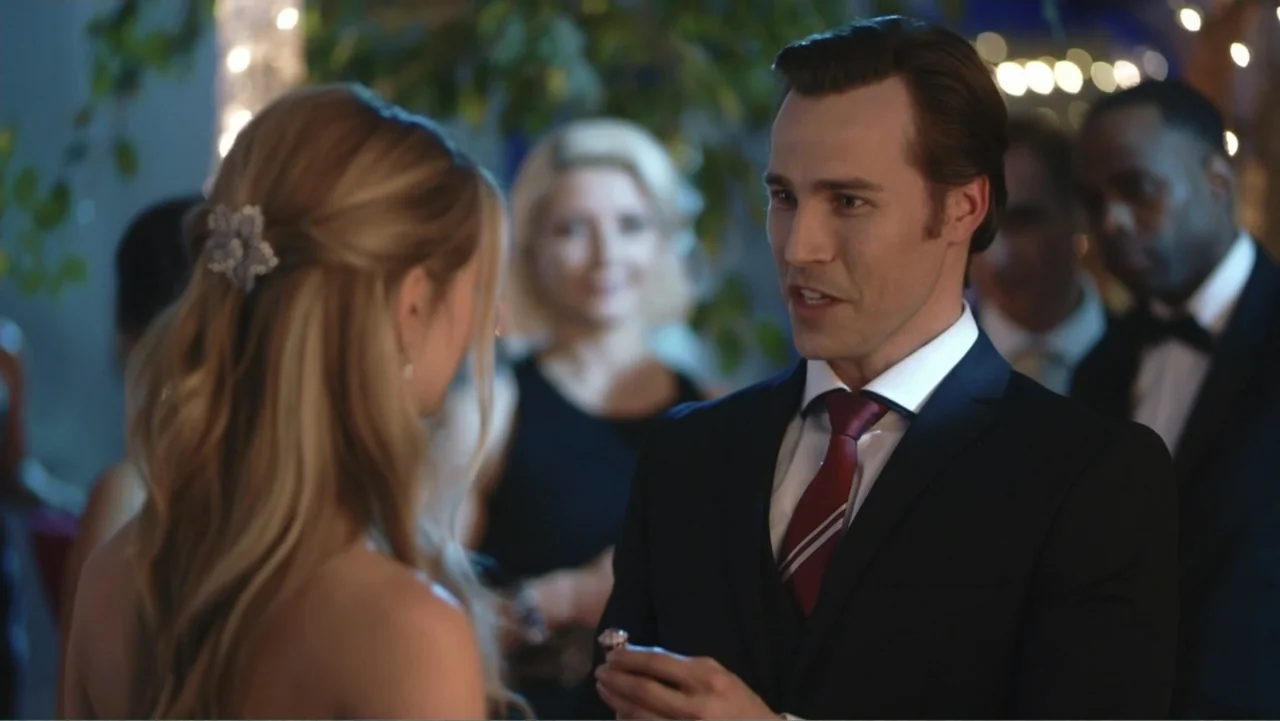 Driving Madeleine (2022) movie still: medium — A man in a tuxedo stands facing a woman in a ballroom. He offers a ring while other guests stand in…