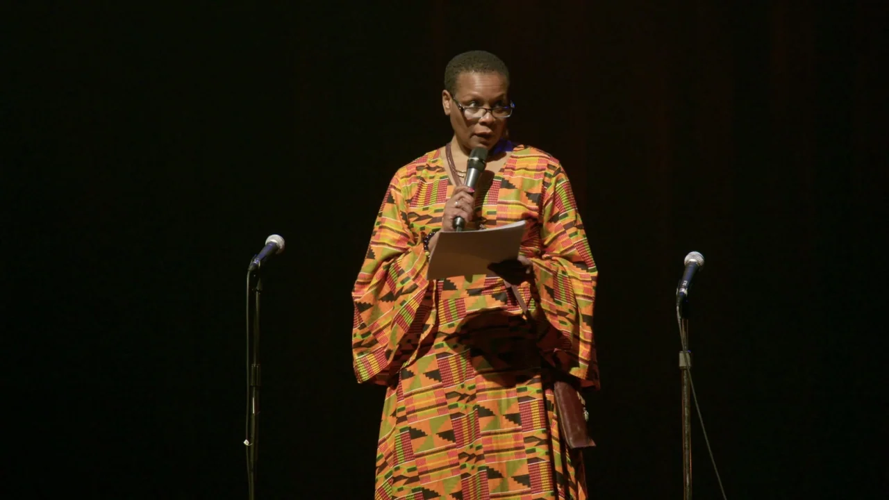 We Are the Dream: The Kids of the Oakland MLK Oratorical Fest (2020) movie still: medium — A woman stands on a darkened stage with two microphone…