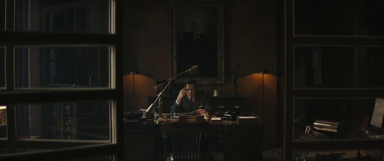 Christopher Robin (2018) movie still: wide — A dimly lit, wood-paneled room features a large, dark-framed portrait hanging on the wall. A man sits…