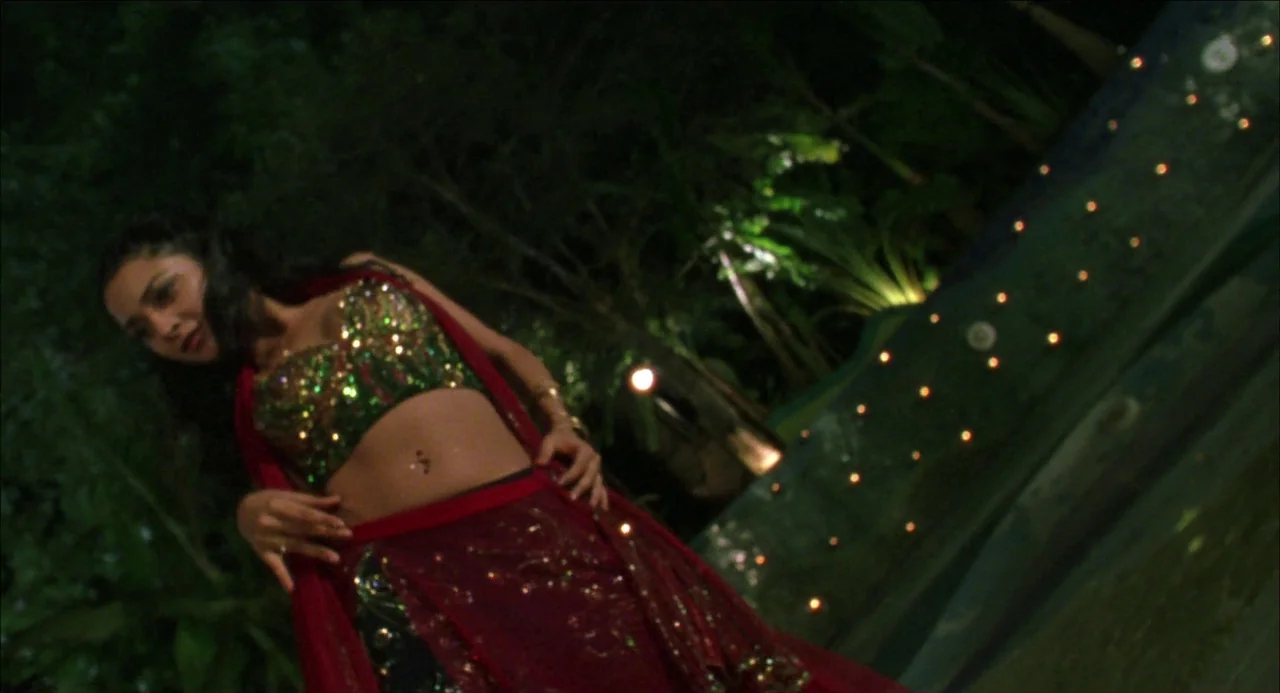 Monsoon Wedding (2001) movie still: medium — A dark outdoor space features a pool bordered by warm, glowing decorative lights. A young woman stands…