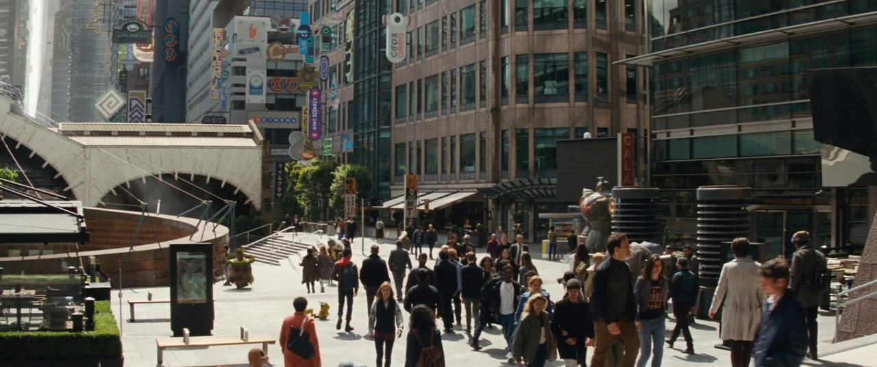 Pokémon Detective Pikachu movie still: wide — A bustling city plaza surrounded by high-rise office buildings featuring neon signage and terraces.…