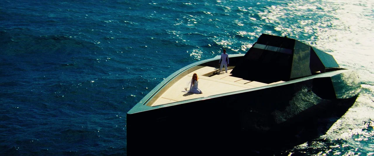 The Island (2005) movie still: wide — A sleek black stealth-like yacht navigates across open dark blue ocean water. A man and a woman in white…