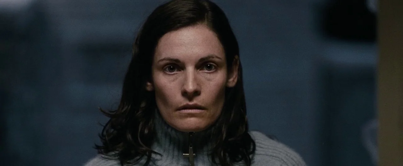 30 Days of Night (2007) movie still: closeup — A dimly lit indoor space with blurred architectural lines in the background. A woman in a grey…