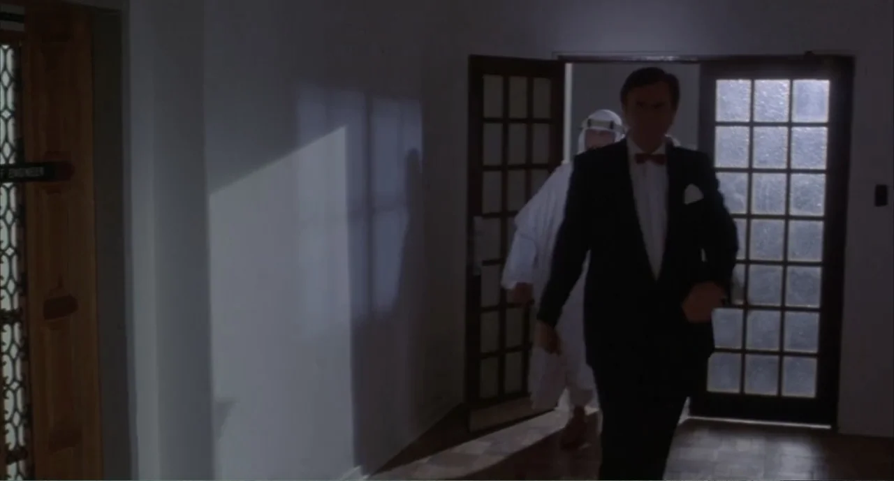 American Ninja 4: The Annihilation (1990) movie still: fullbody — A modern building corridor features white walls and glass-paned wooden doors. A…