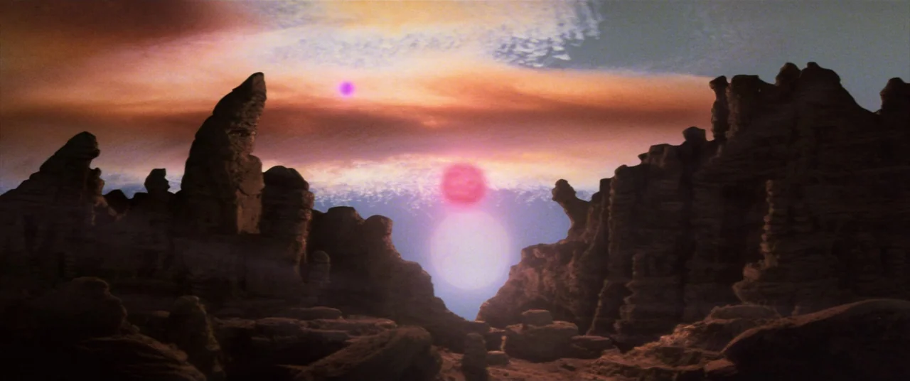 The Dark Crystal (1982) movie still: establishing — A rocky desert landscape sits under a sky with multiple glowing celestial objects. Dark stone…