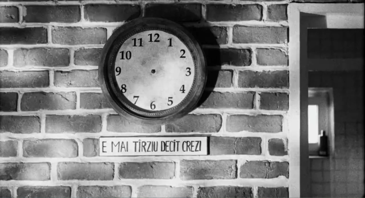 Do Not Expect Too Much from the End of the World (2023) movie still: medium — A brick wall interior features a large round wall clock and a…