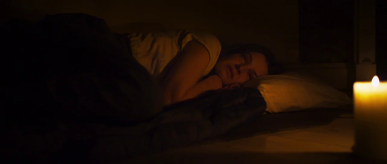 A Dark Song (2016) movie still: medium — A dark, sparsely furnished space features a person lying on a floor-level mattress. The only light source…
