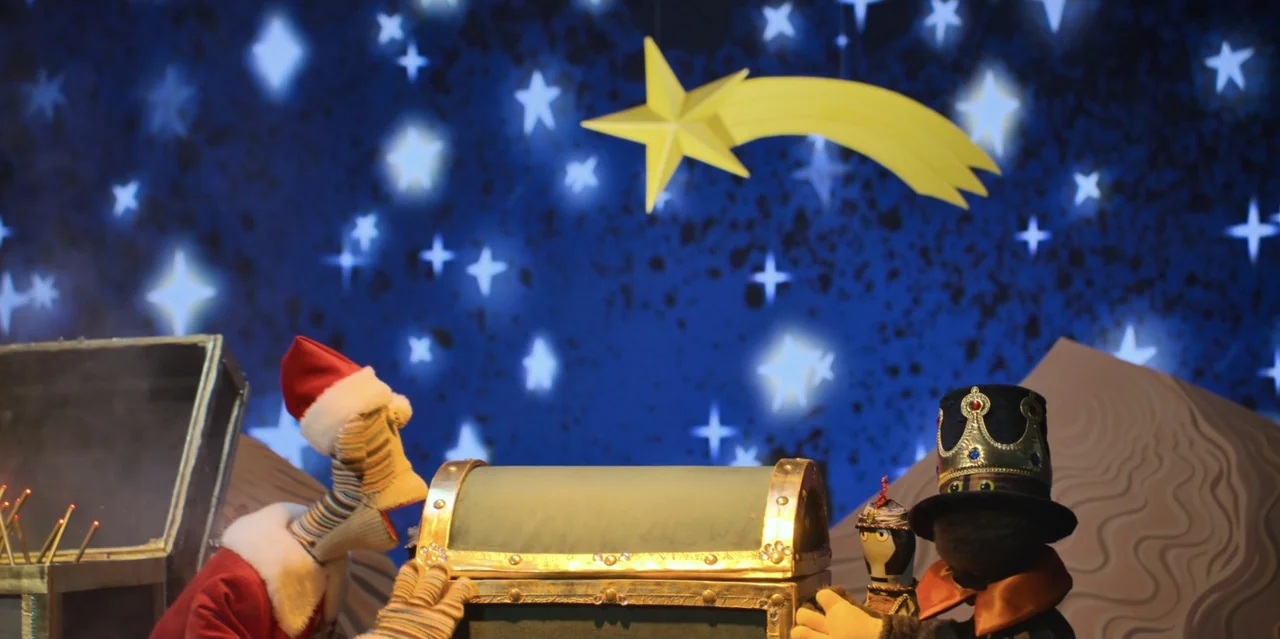 31 Minutes: One Hot Christmas (2025) movie still: medium — A miniature stage features a decorated chest placed in front of a painted starry sky. Two…