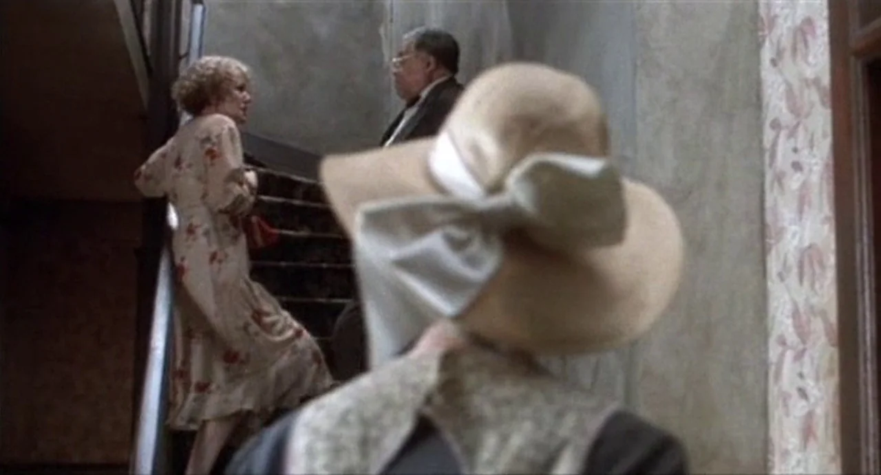 The Annihilation of Fish (1999) movie still: medium — An indoor staircase features textured off-white walls with a floral patterned border. A woman…