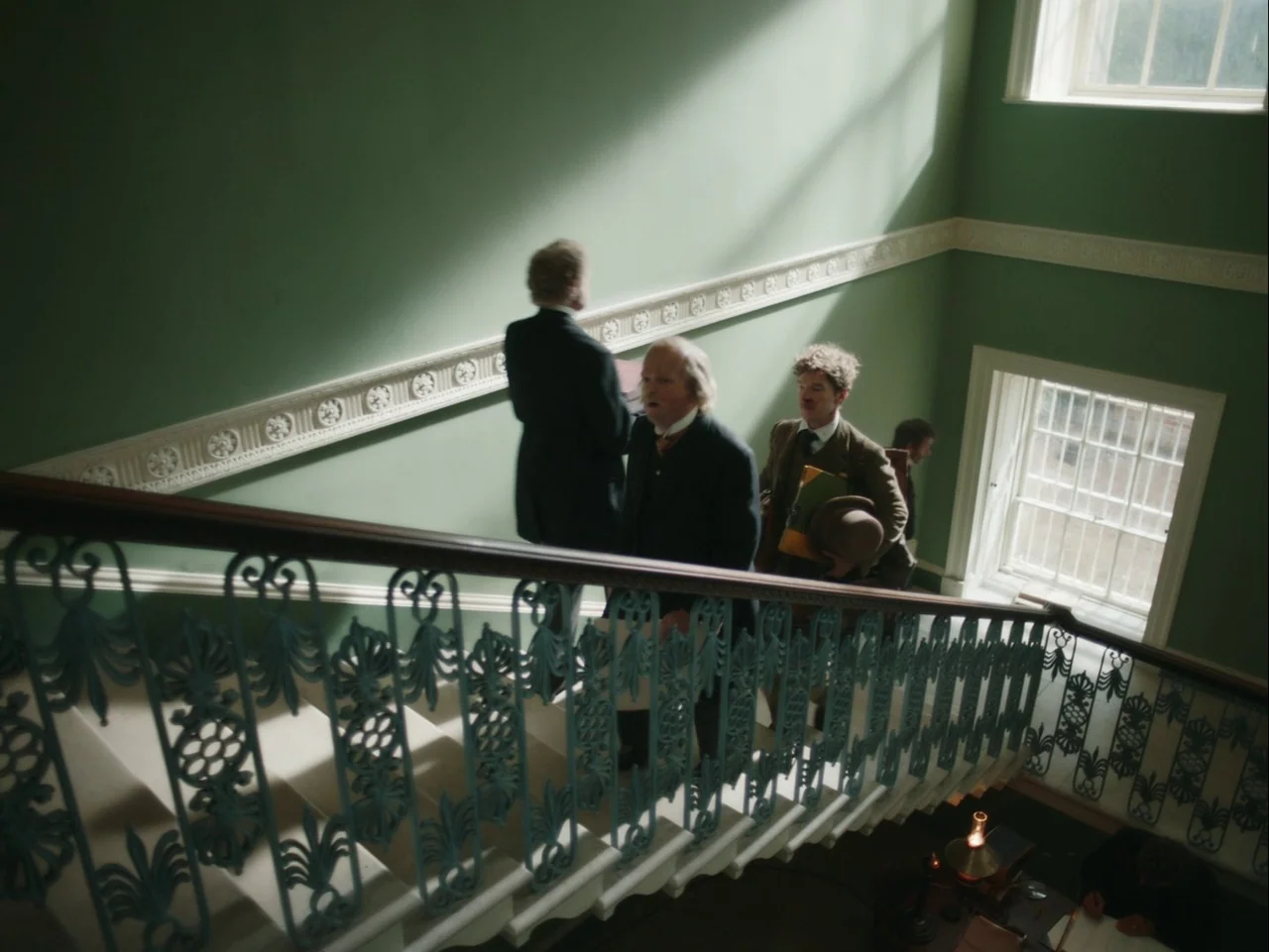 The Electrical Life of Louis Wain (2021) movie still: medium — A historic interior staircase features ornate iron railings and pale sage green…