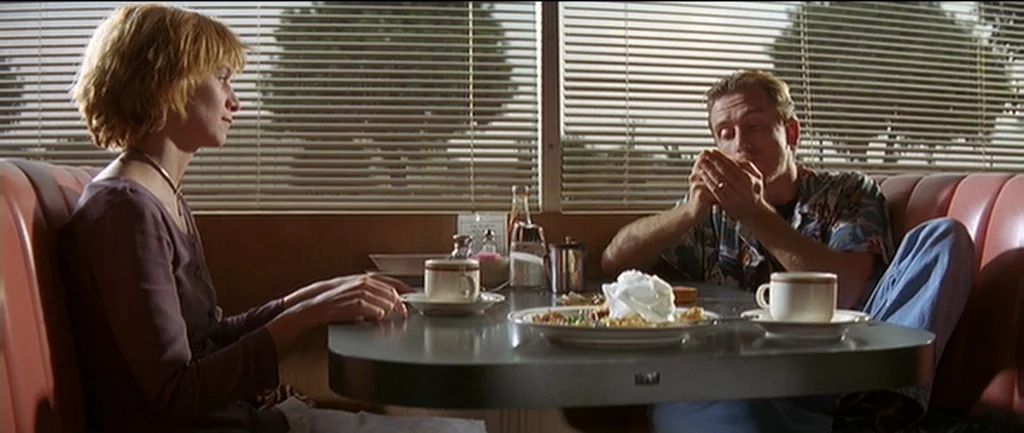 Pulp Fiction (1994) movie still: medium — A diner booth with red vinyl seats and a grey laminate table. A woman and a man sit opposite each other…