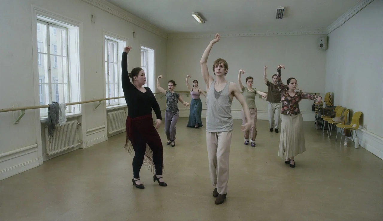A Pigeon Sat on a Branch Reflecting on Existence (2014) movie still: fullbody — A spacious room with beige flooring, white walls, and large windows…