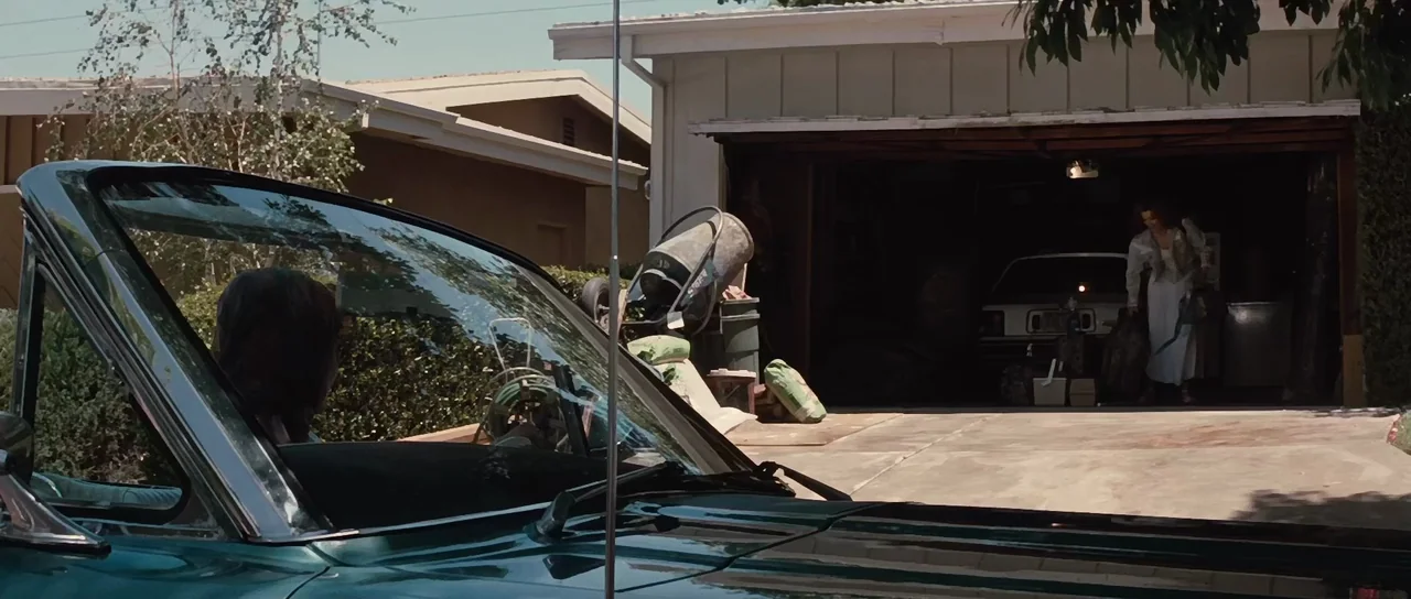 Thelma & Louise (1991) movie still: wide — A residential driveway with a suburban house, a garage, and a parked car. A woman walks out of the dark…