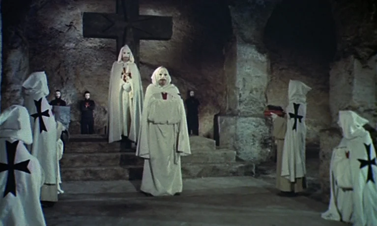 Nuits Rouges (1974) movie still: fullbody — A dark subterranean stone crypt features a large carved cross against the back wall. Several figures…