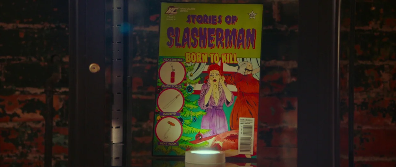 Random Acts of Violence (2019) movie still: closeup — A comic book titled Slasherman stands upright inside a darkened glass display case. The bright…