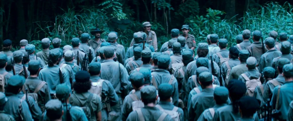 Che Part 1 (The Argentine) (2008) movie still: wide — A large group of soldiers in olive uniforms stands in a dense jungle clearing. Two men in…