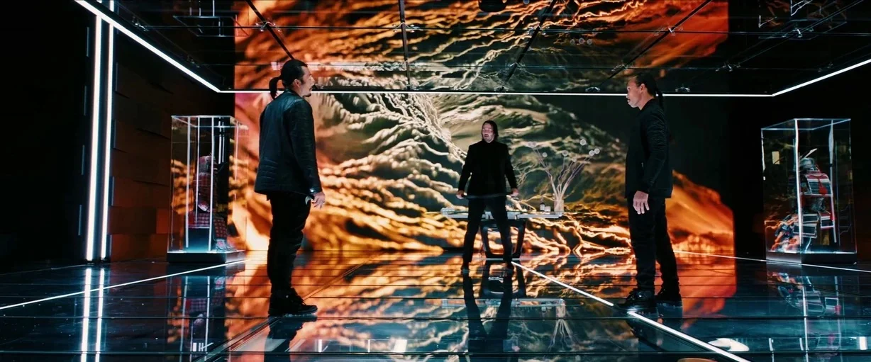 John Wick (2014) movie still: wide — A high-tech gallery with glossy floors contains glass display cases housing samurai armor sets. Three men stand…