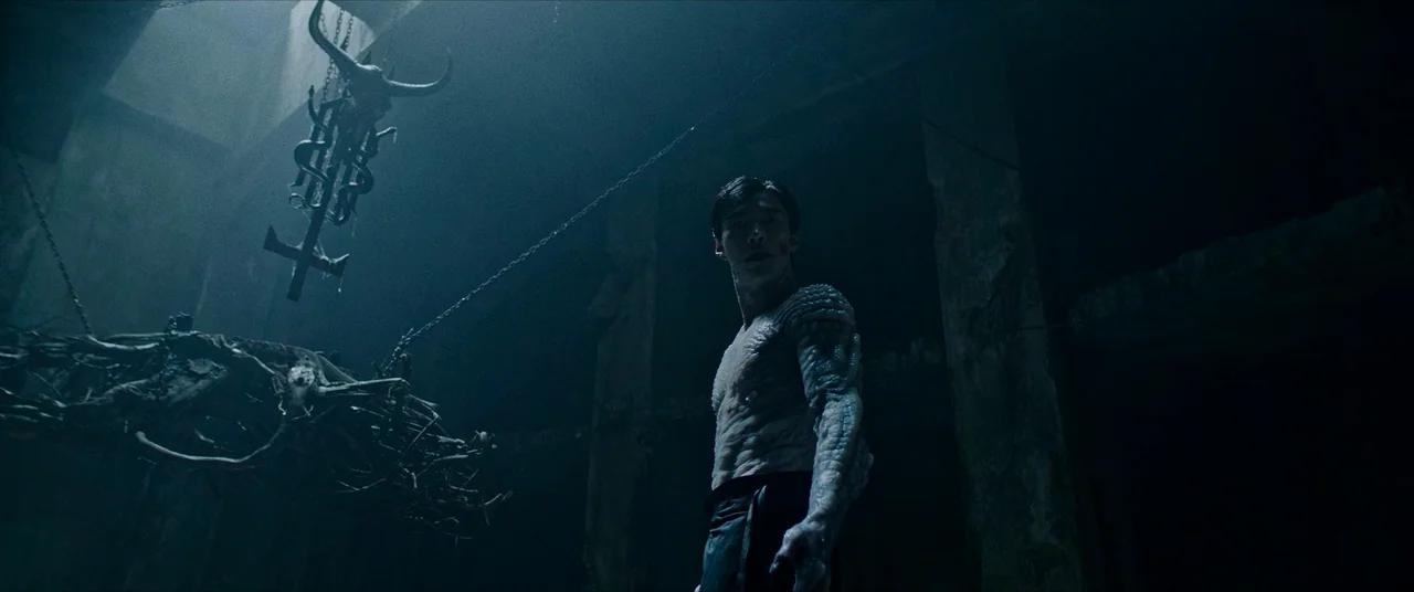The Divine Fury (2019) movie still: medium — A dark subterranean chamber contains a metallic bull-skull emblem hanging from heavy chains. A…