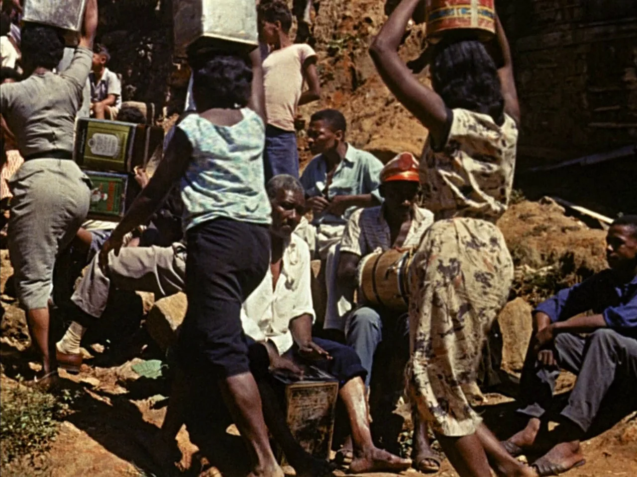 Black Orpheus (1959) movie still: fullbody — A group of people gathers on a dry, rocky hillside with loose dirt. Several individuals carry boxes on…