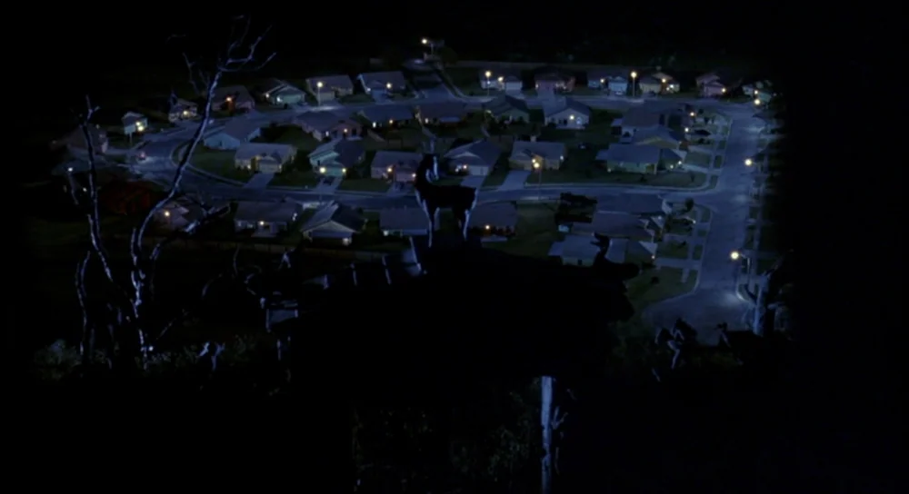 Edward Scissorhands (1990) movie still: establishing — An aerial night view of a suburban neighborhood shows winding streets and small homes. The…