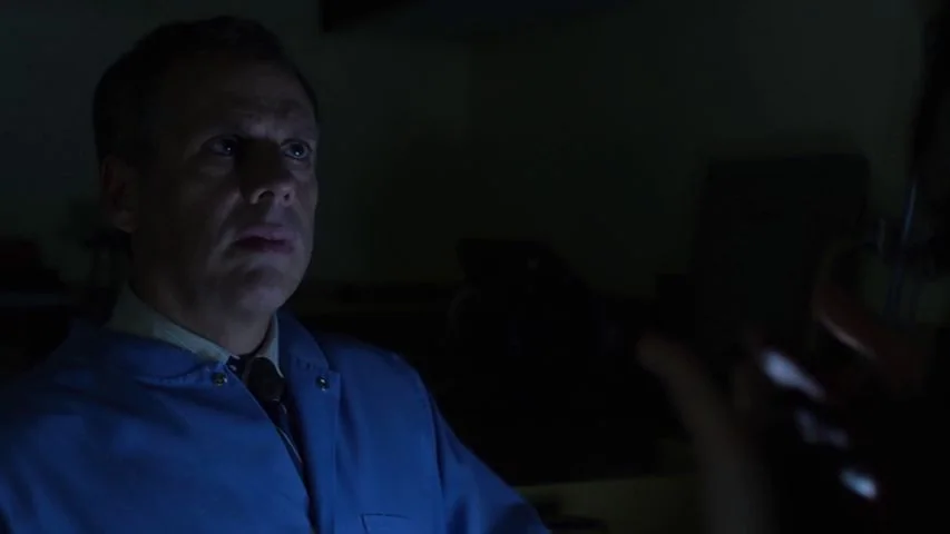 Touchy Feely (2013) movie still: medium — A dark environment with minimal visible furniture in the deep background. The man faces slightly right…