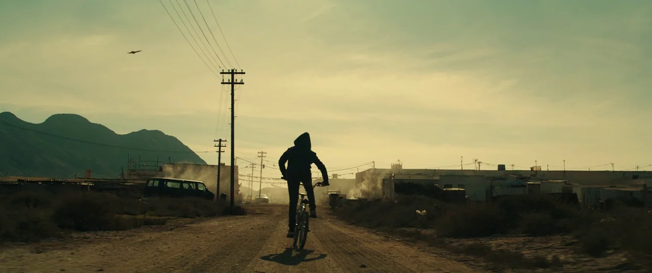 Assassin’s Creed (2016) movie still: wide — A dusty dirt road stretches through a sparse, dry landscape with distant mountains. A lone figure in a…