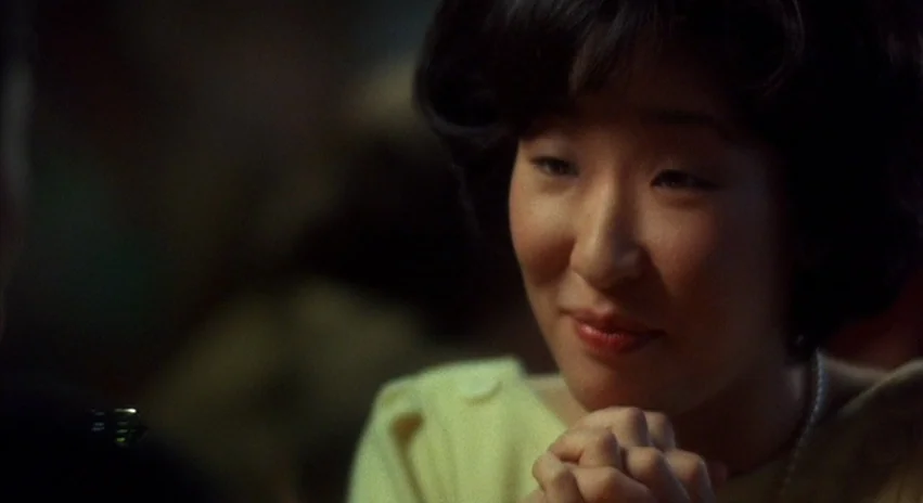 Double Happiness (1994) movie still: closeup — A dimly lit restaurant interior provides a dark backdrop for the subject. A woman sits at a table…